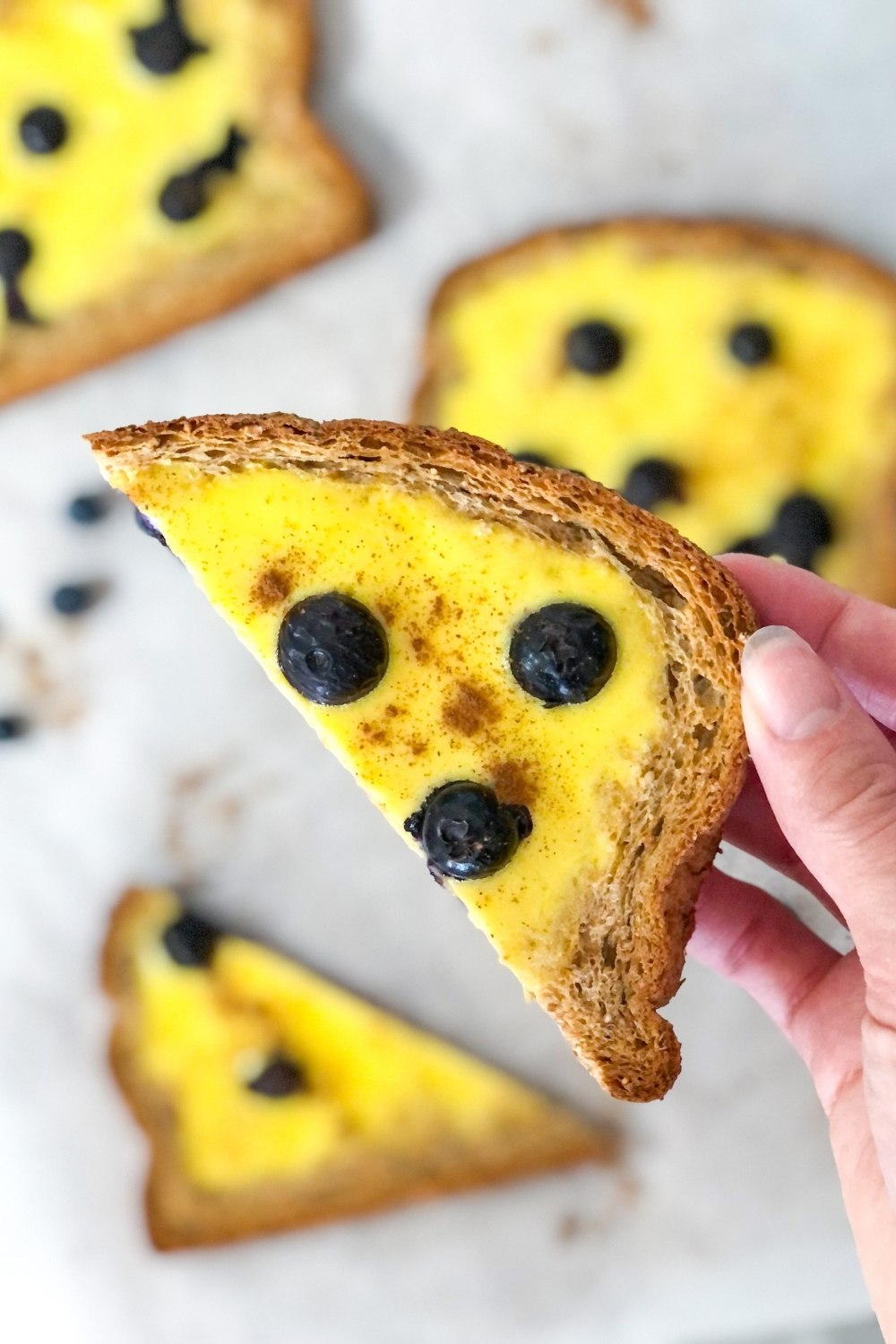 a piece of custard yogurt toast with blueberries being held up with the background out of focus