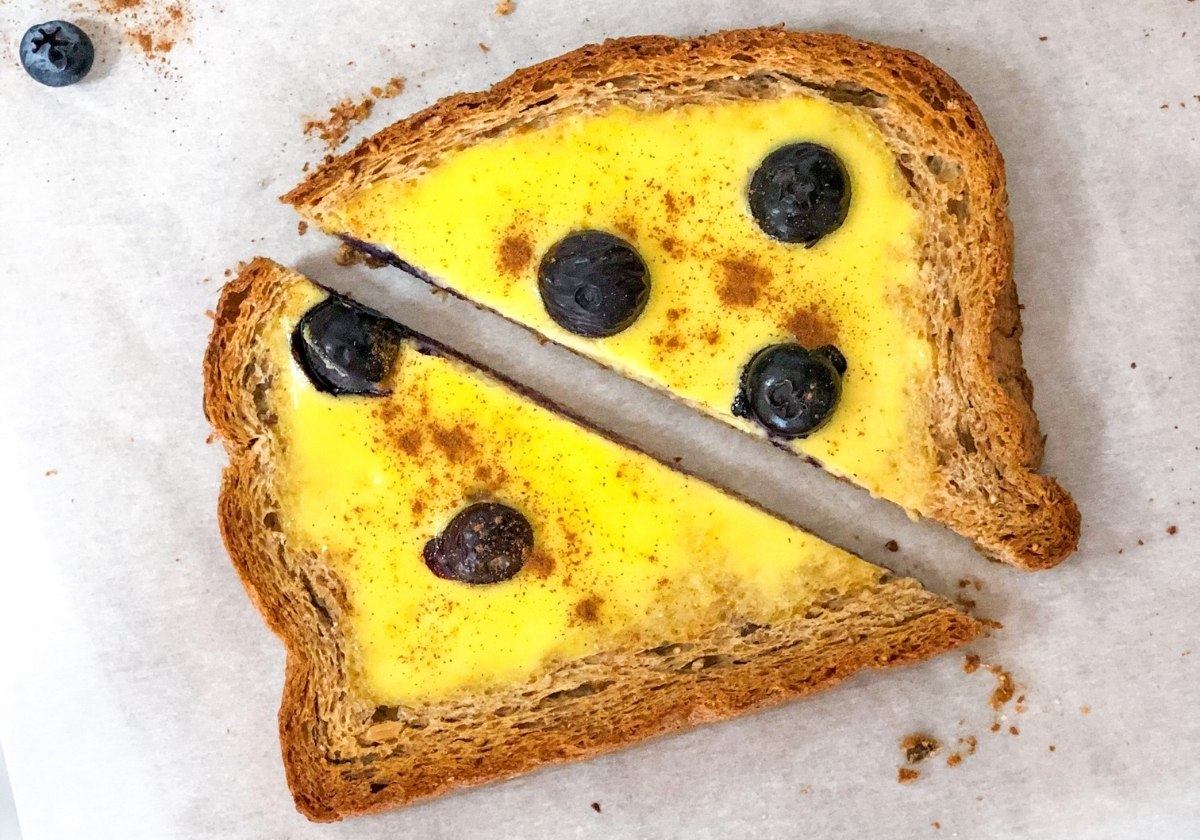 a piece of custard yogurt toast with blueberries being held up with the background out of focus