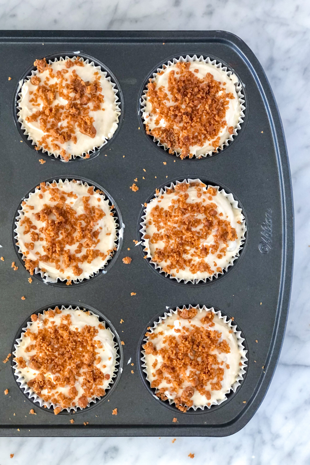 no bake mini biscoff cheesecakes in a muffin tin topped with crushed lotus biscoff cookies