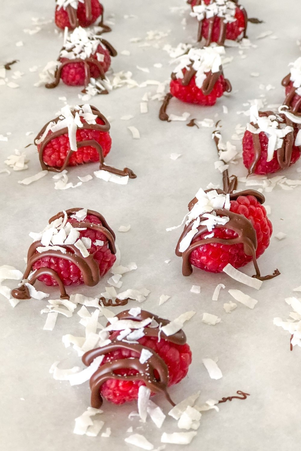 raspberries with chocolate drizzle and coconut on parchment paper