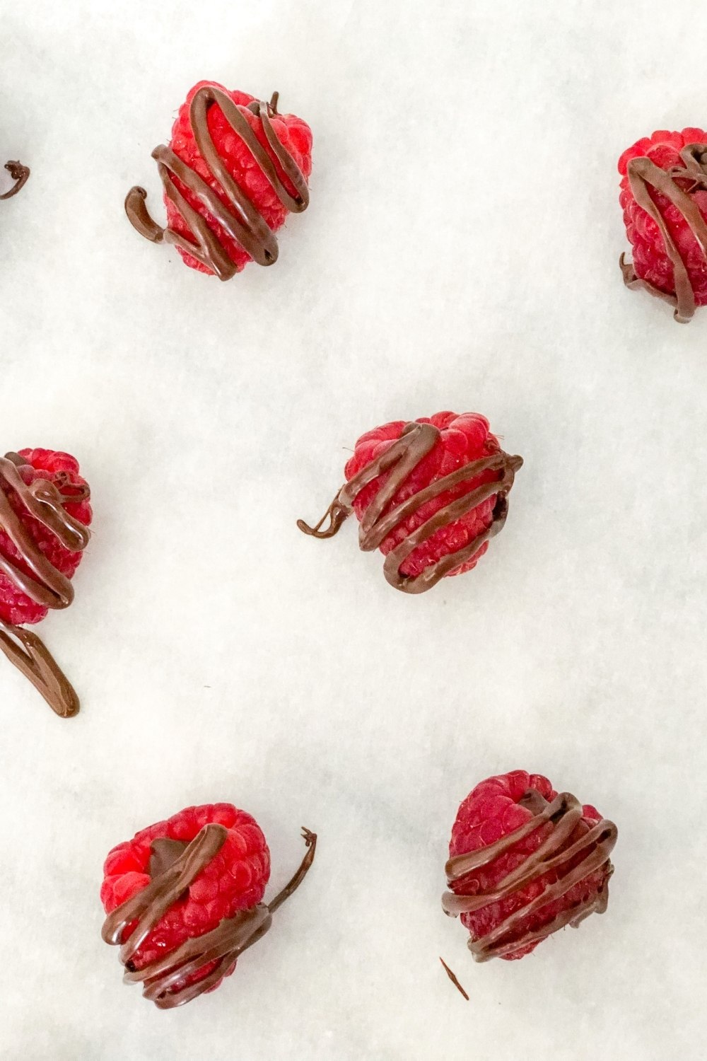 raspberries with chocolate drizzle on parchment paper