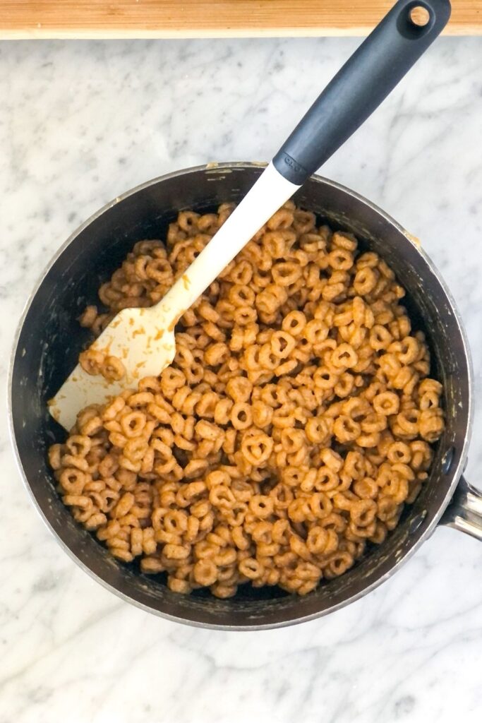 honey peanut butter cheerio mixture in a saucepan with a small spatula