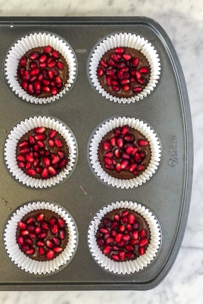 pomegranate seeds on melted dark chocolate in cupcake liners