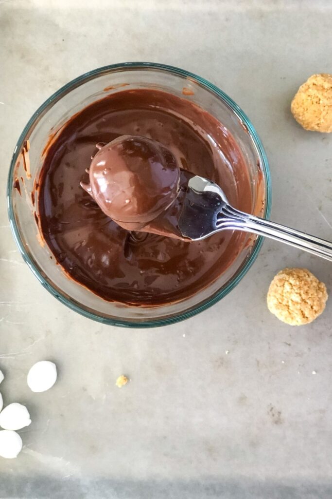 dipping smores truffle balls into melted chocolate with a fork