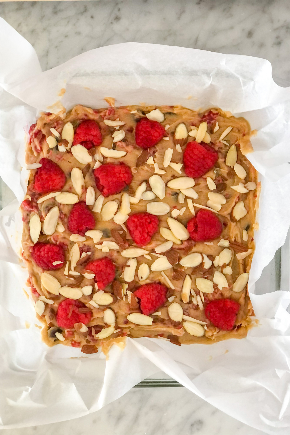 blondie batter in baking pan topped with raspberries and slivered almonds