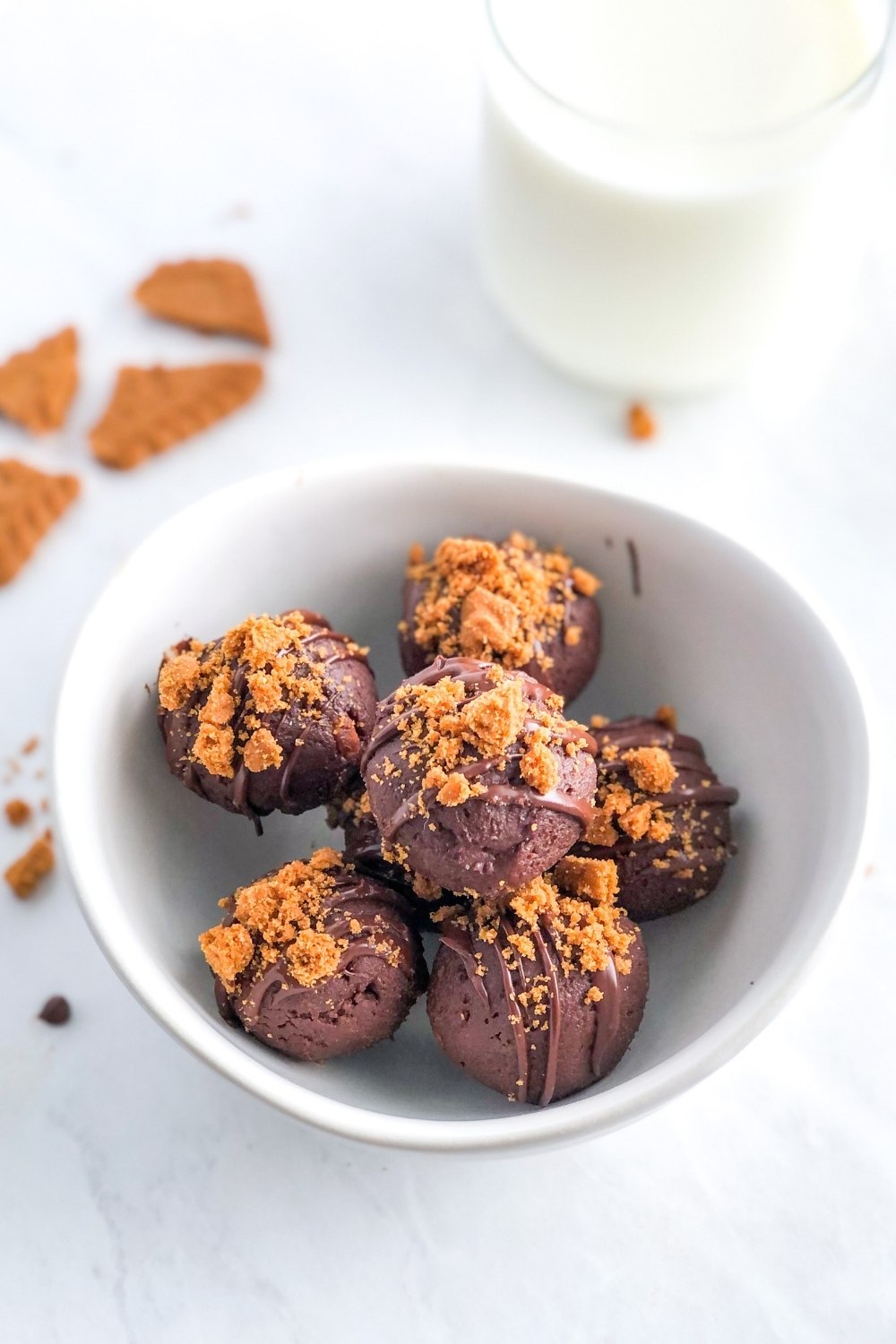 chocolate Biscoff truffles in a white bowl with a glass of milk