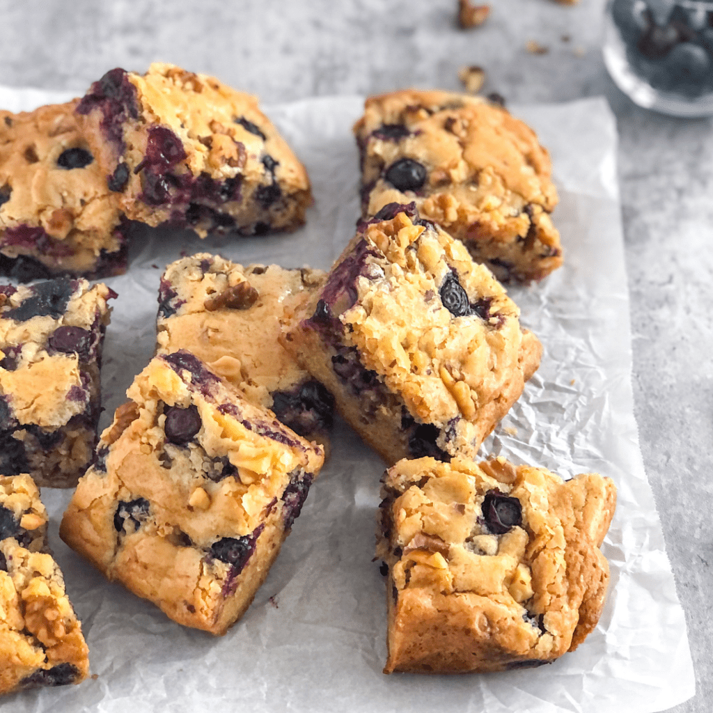 a pile of blueberry walnut blondie bars on white parchment paper