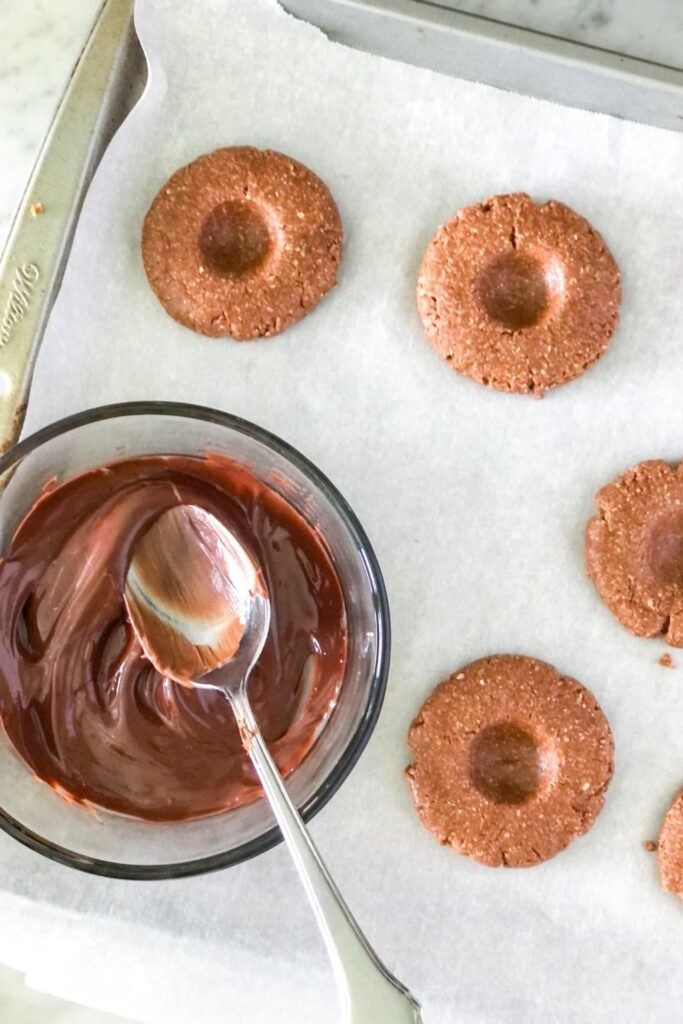 no bake oat flour thumbprint cookies with a bowl of melted chocolate and nutella on parchment paper