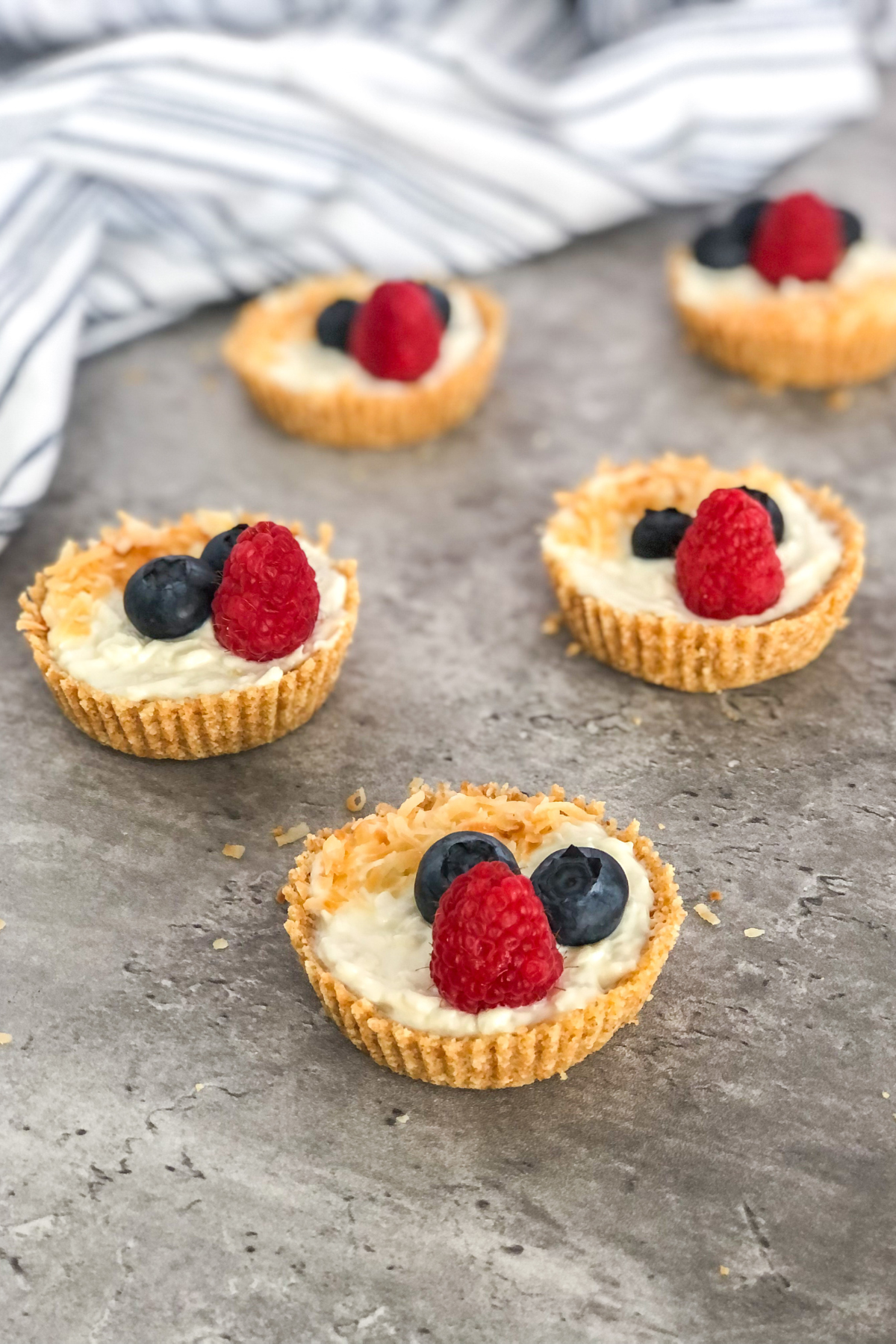 mini coconut tarts with yogurt and berries in front of a white and blue striped kitchen towel