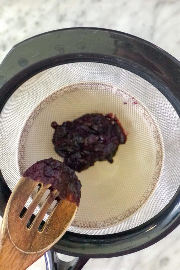 blueberry sauce in a sieve with a bowl underneath