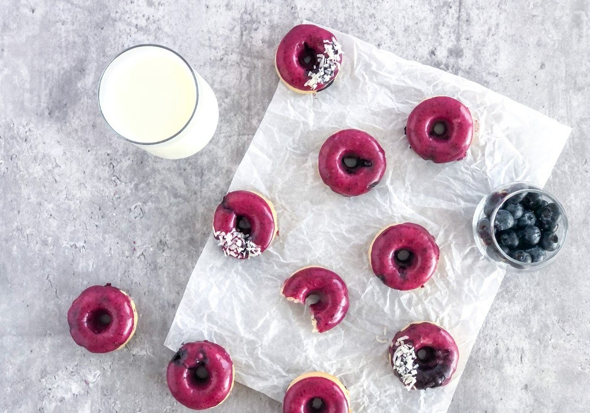 mini baked blueberry glazed donuts on parchment paper with a glass of milk