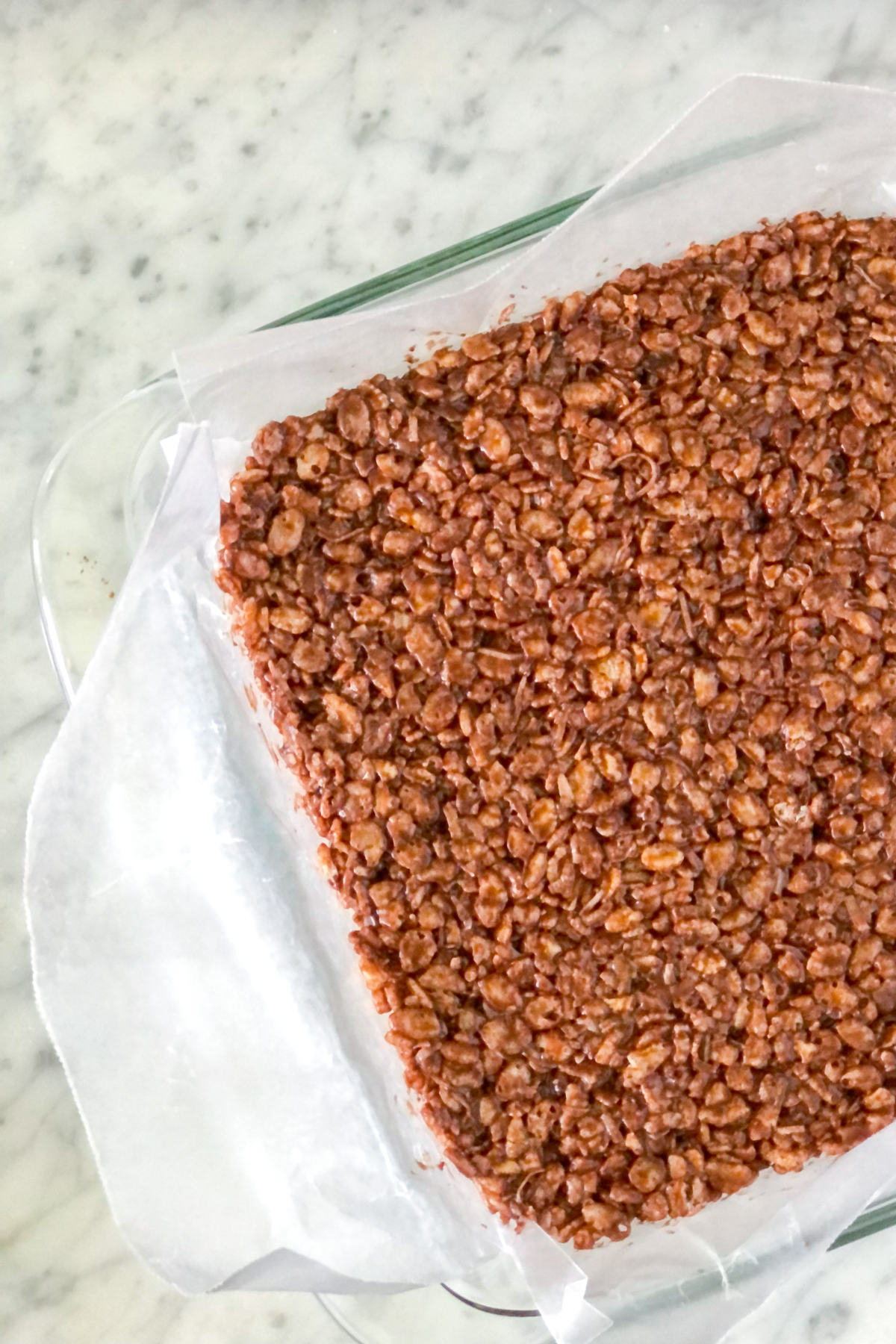 cocoa powder and rice krispies with melted marshmallows in a square baking pan