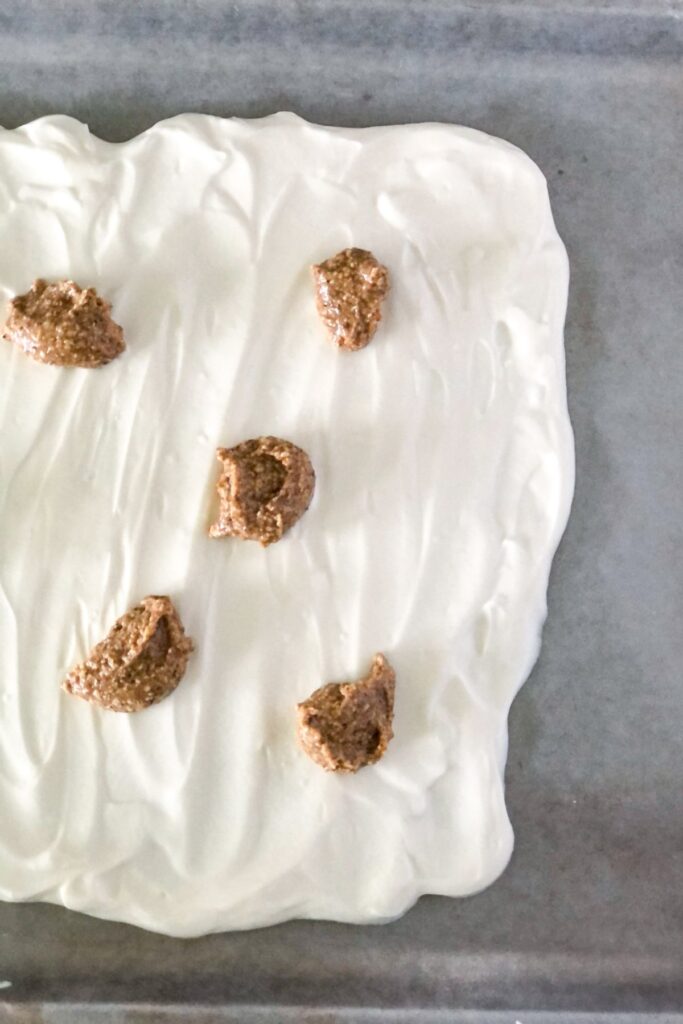 spoonfuls of almond butter on yogurt mixture spread out on sheet pan