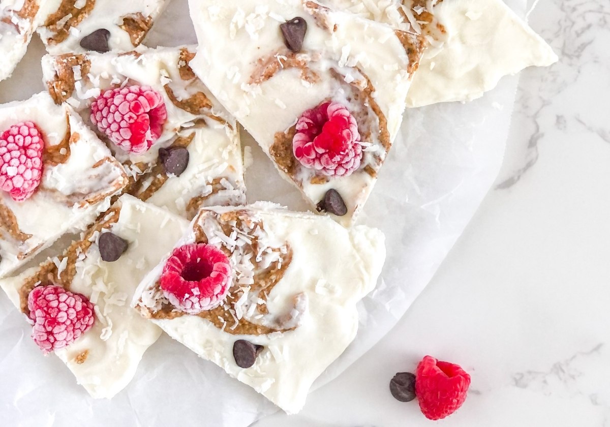 almond butter frozen yogurt bark with raspberries on parchment paper