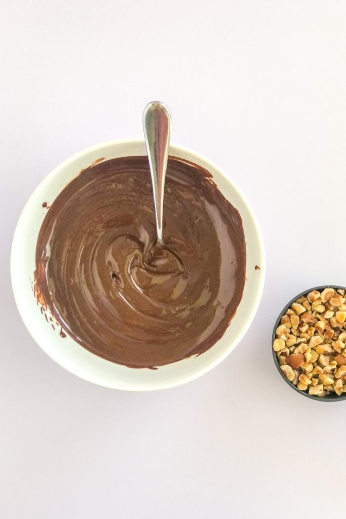 melted chocolate and Nutella in a bowl next to a measuring cup filled with hazelnuts