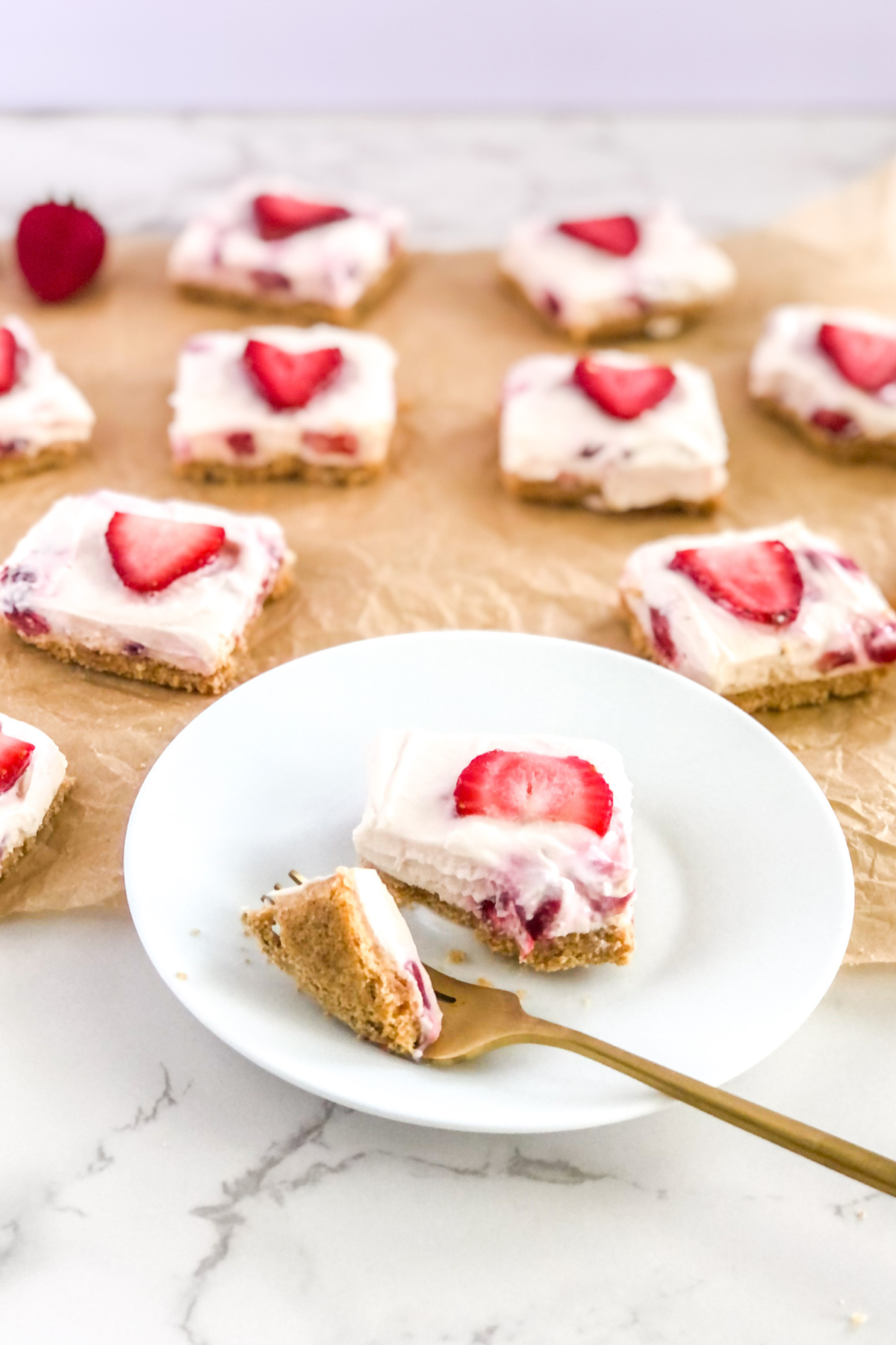 strawberry cheesecake with graham cracker crust on a white plate with a gold fork