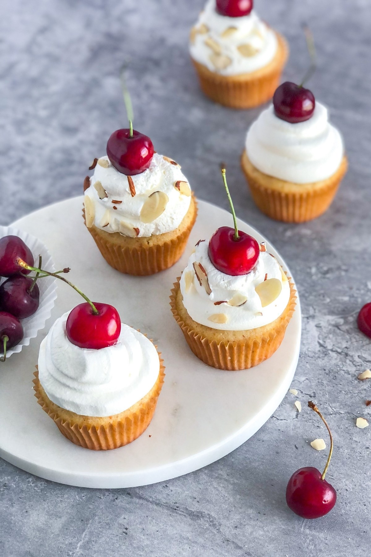 cherry cupcakes on a circular white marble platter with fresh cherries and sliced almonds
