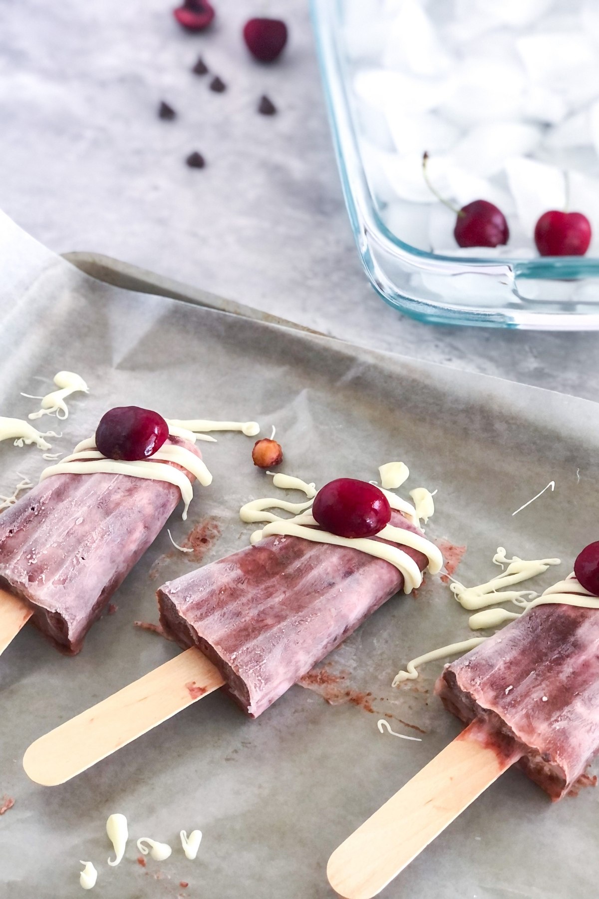 chocolate cherry popsicles with white chocolate drizzle on a sheet pan