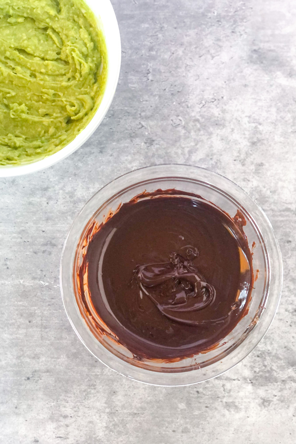 melted chocolate in a bowl next to a bowl with mashed avocado