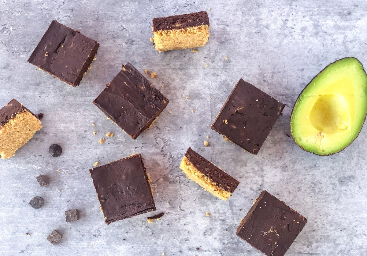 chocolate avocado bars with graham cracker crust next to an avocado half on a grey surface