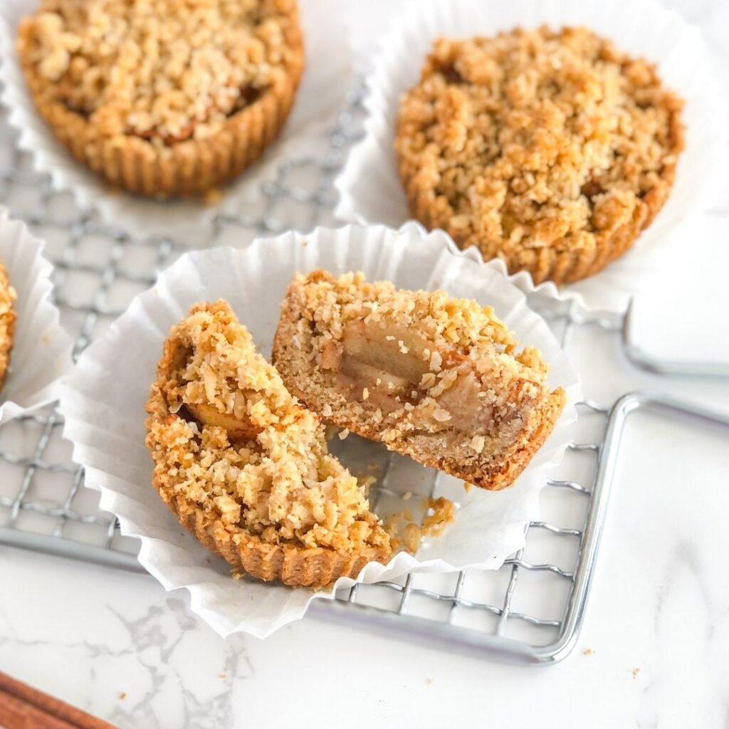 A mini apple tart with crumb topping cut in half on a white paper muffin liner