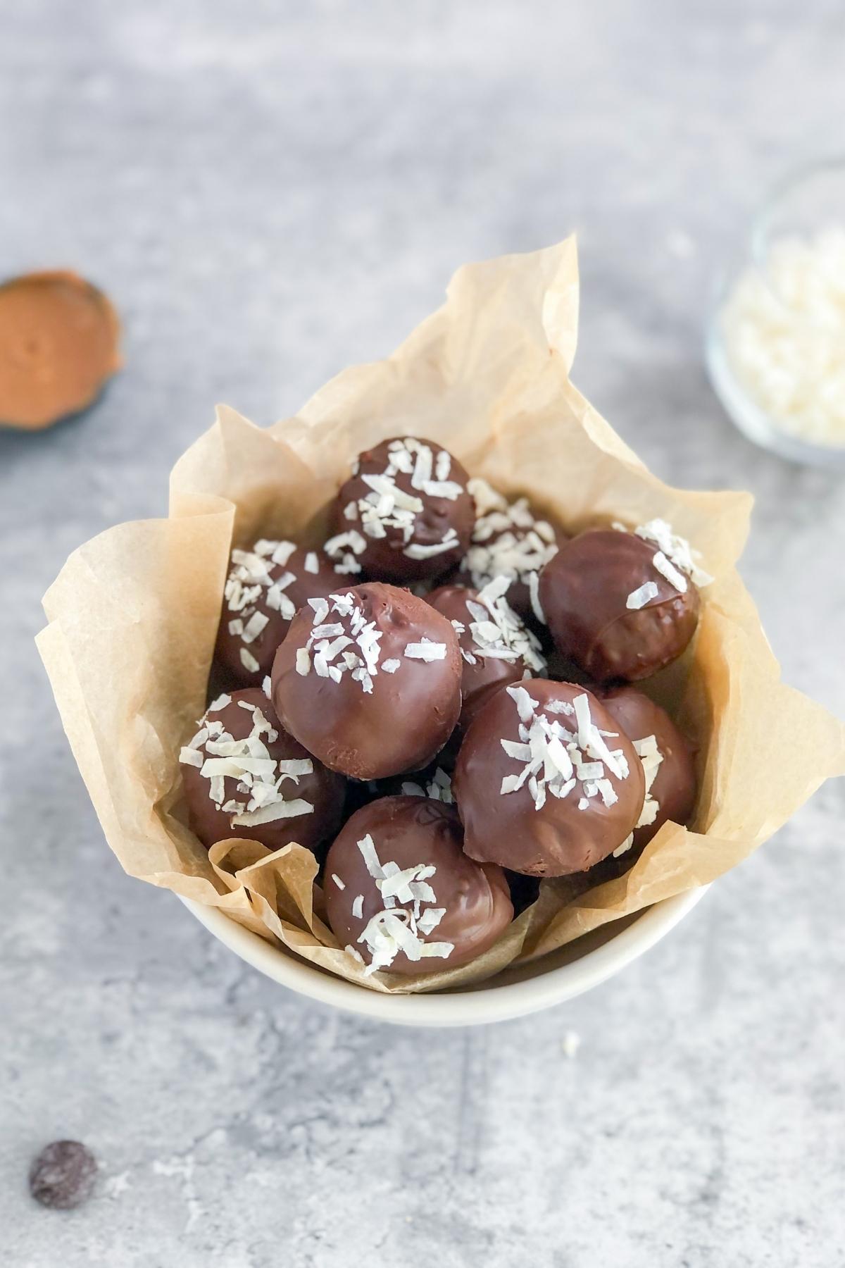 dark chocolate coconut bites in a bowl with a spoon of almond butter