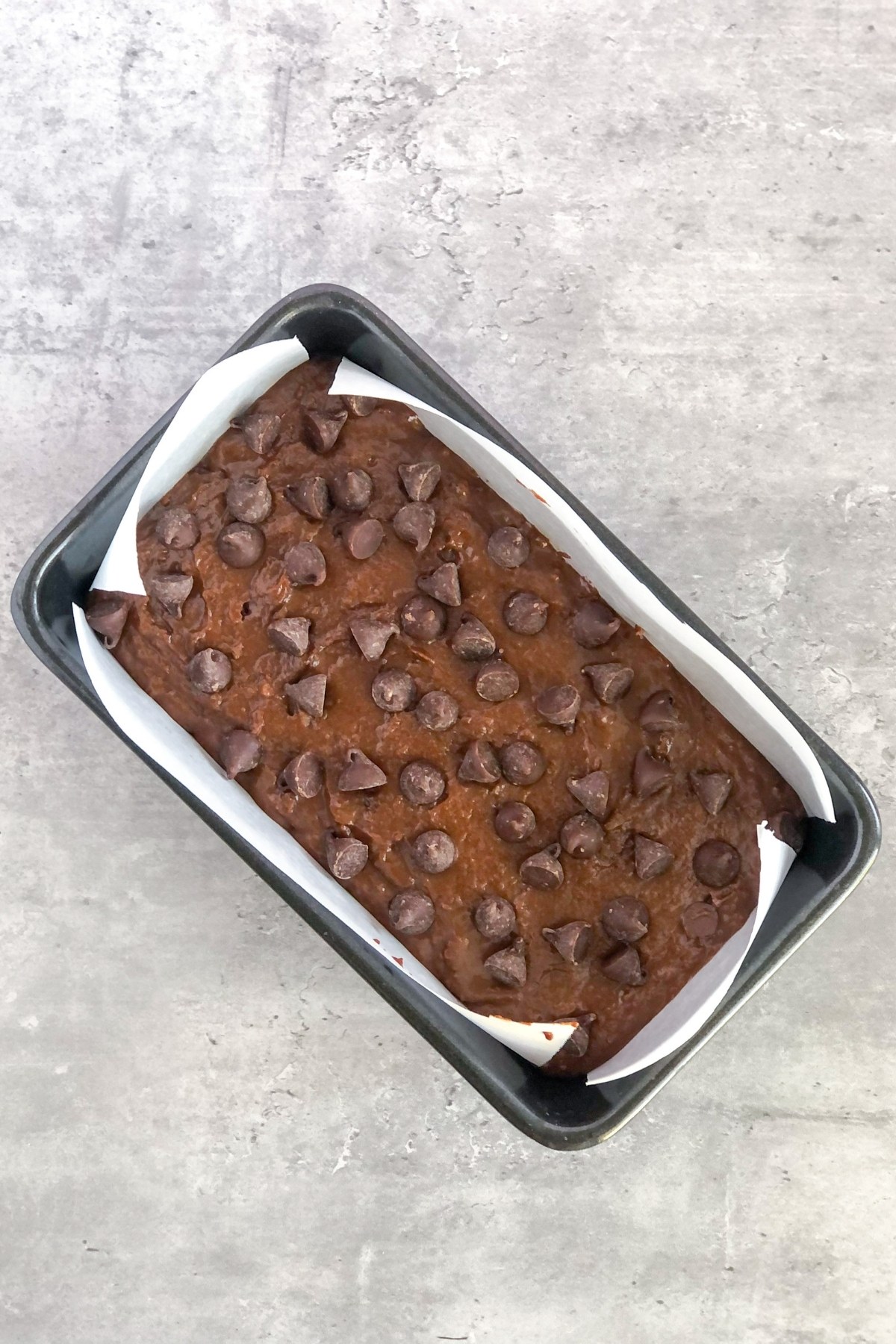 chocolate bread batter in a loaf pan with chocolate chips on top