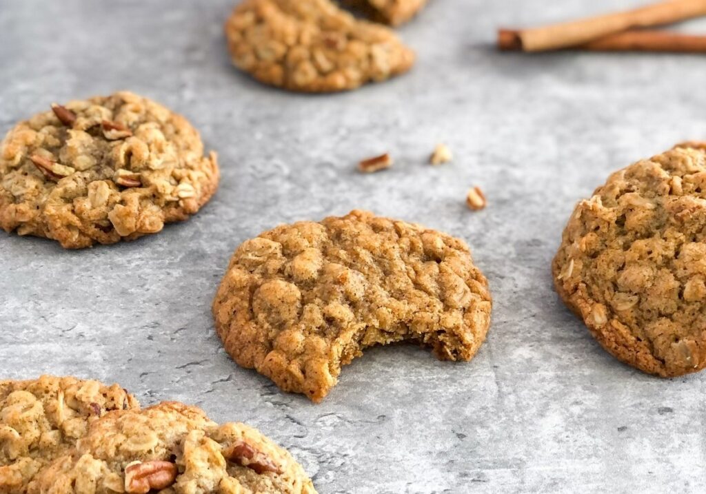 spiced oatmeal cookies with pecans next to cinnamon sticks on a grey background