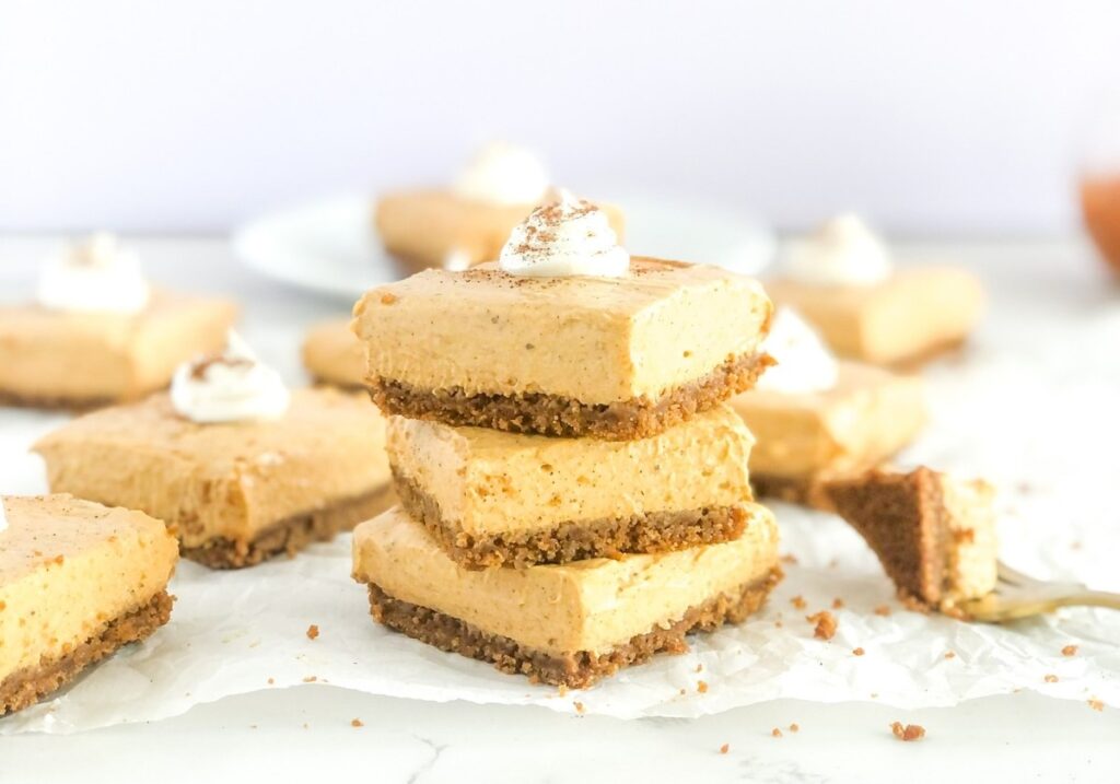 stack of pumpkin cheesecake bars with whipped cream and cinnamon on top