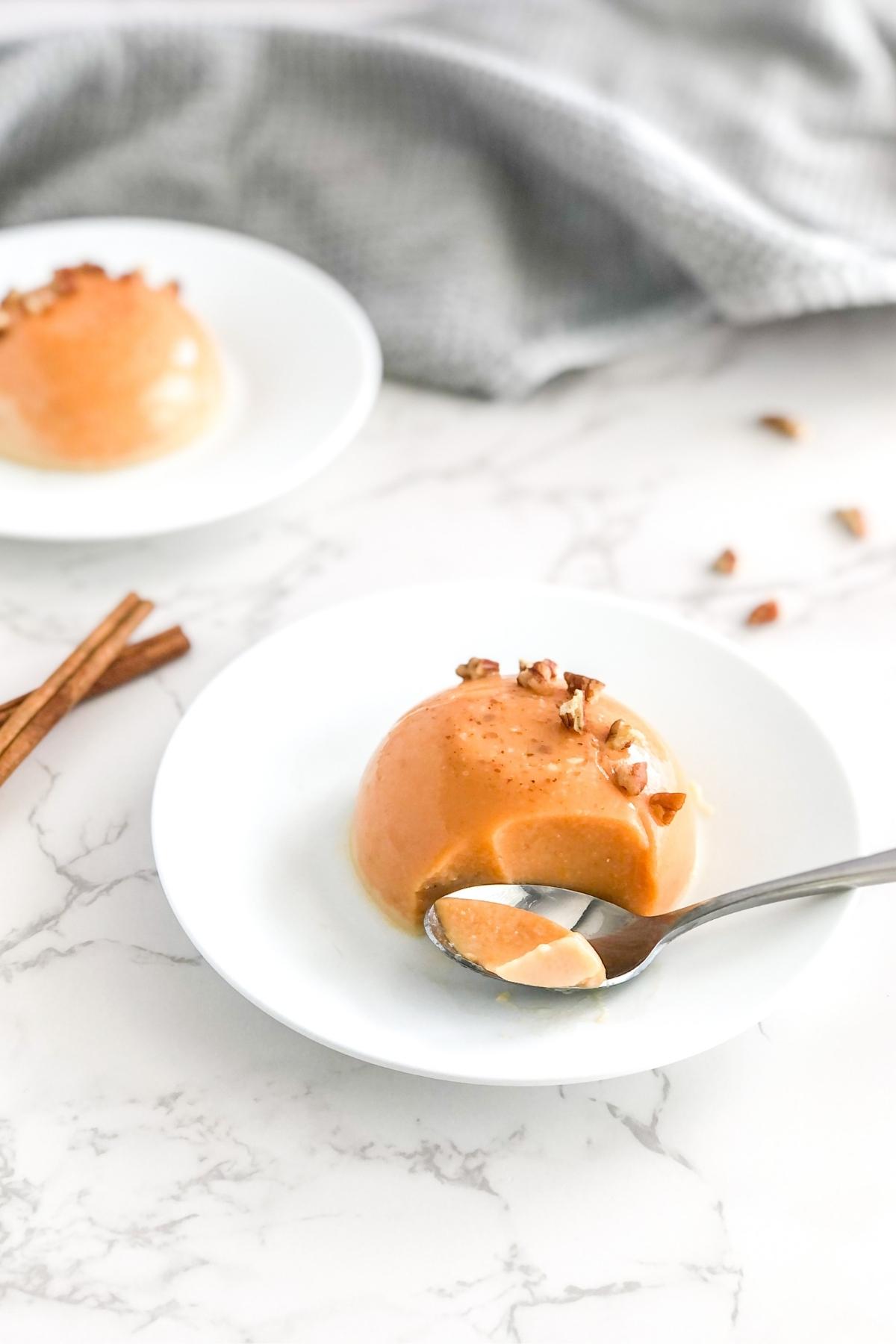maple syrup pumpkin panna cotta with pecans on a plate with a spoon