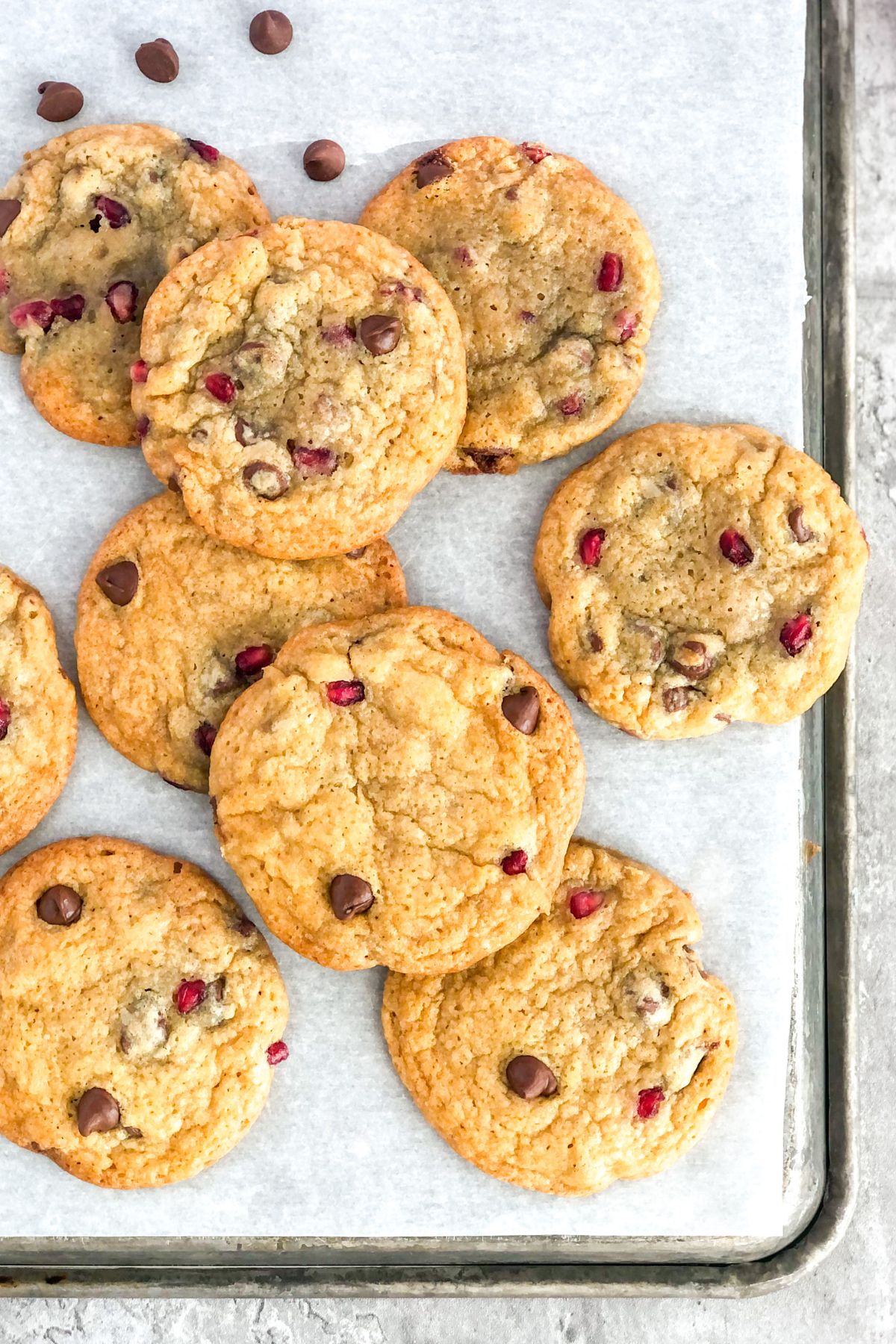 chocolate chip cookies with pomegranate seeds on a metal sheet pan with parchment paper