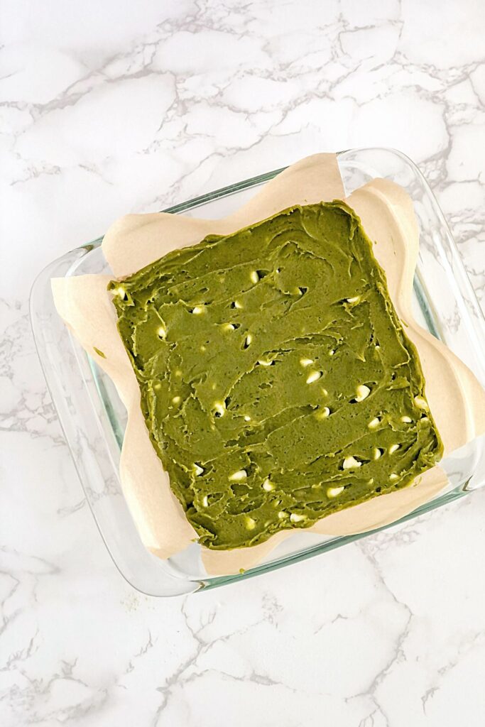 matcha brownie batter with white chocolate chips in a glass baking pan