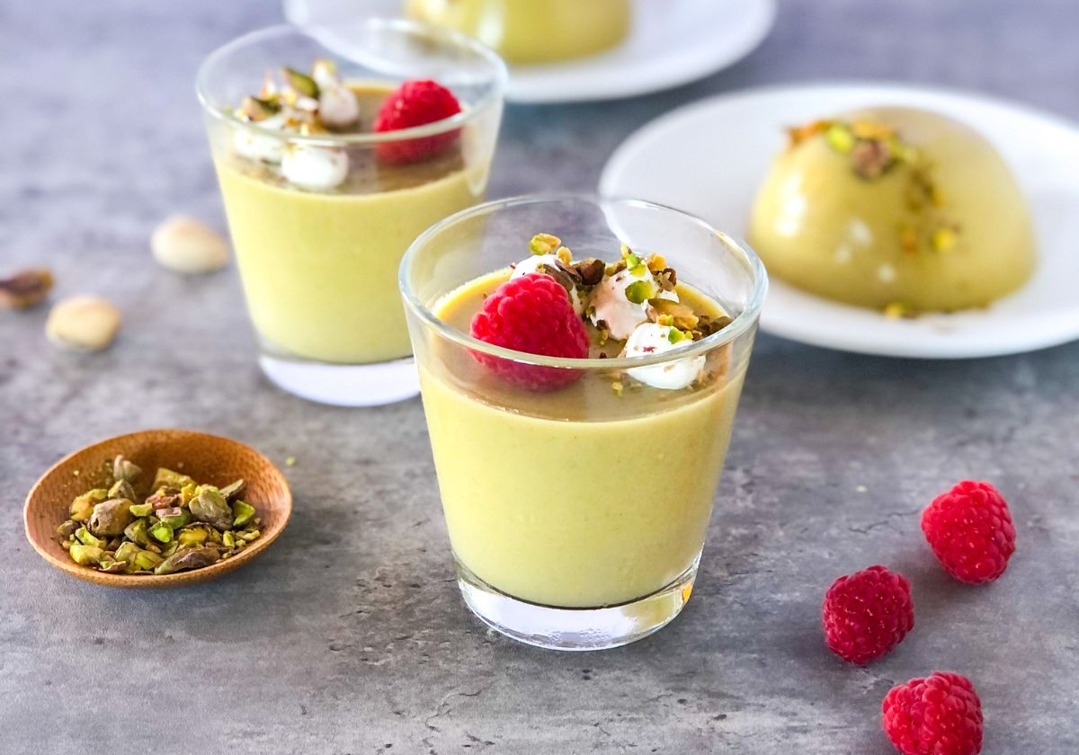maple pistachio panna cotta in small jars with whipped cream and raspberries