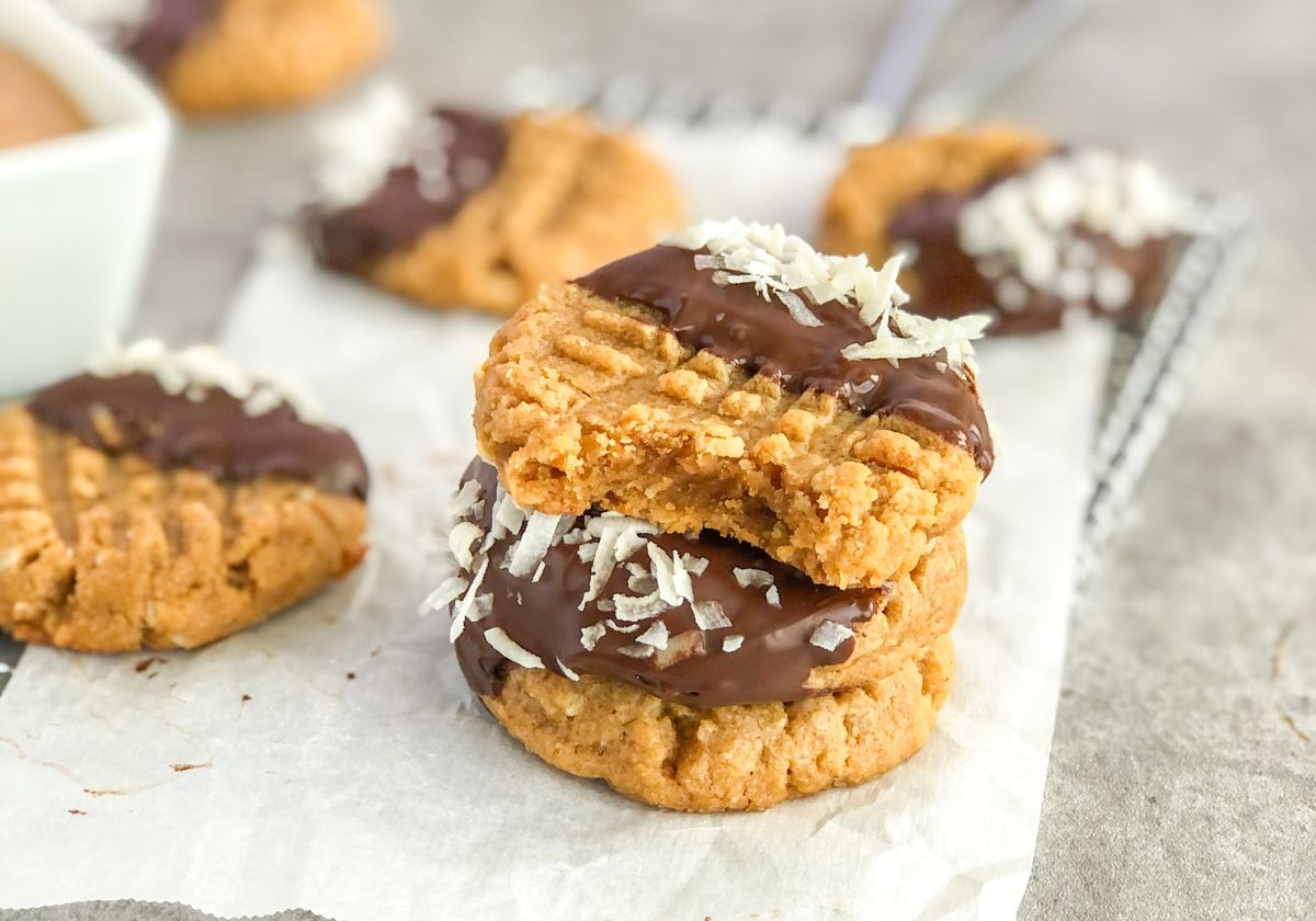 a stack of peanut butter coconut cookies dipped in melted chocolate on parchment paper