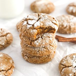 stack of ginger molasses crinkle cookies on parchment paper with a glass of milk