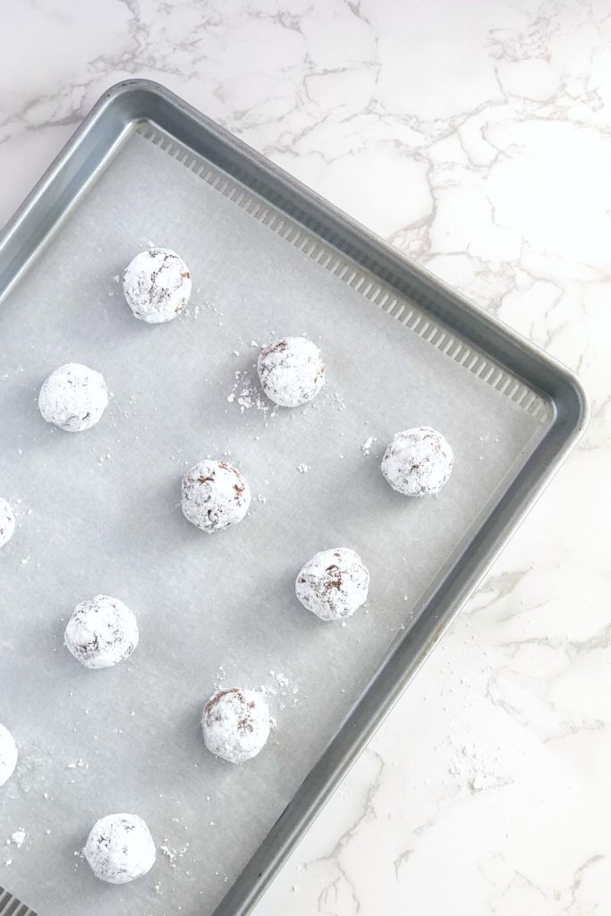 cookie dough balls rolled in powdered sugar on a baking sheet