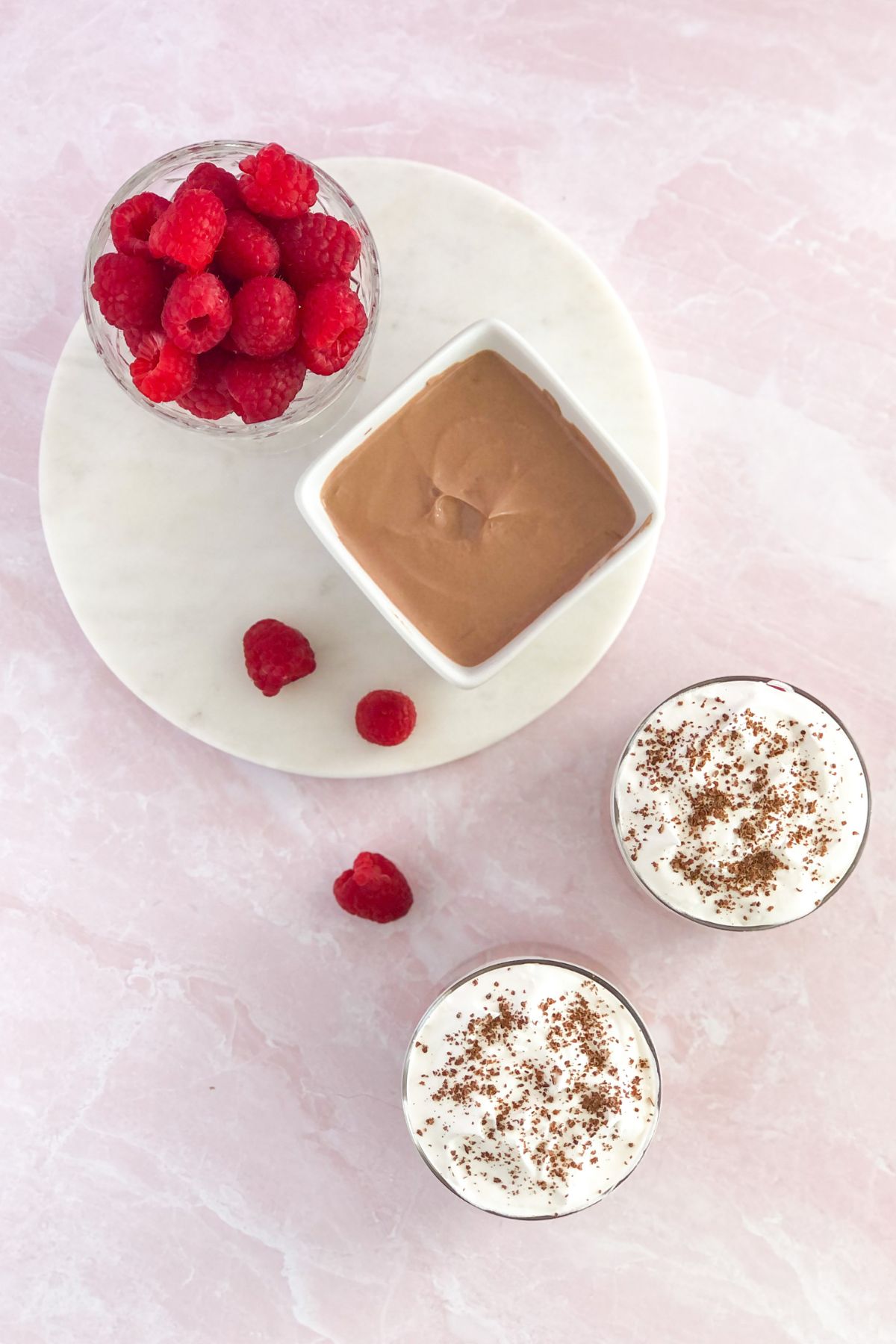 yogurt with cocoa powder in a white square bowl with raspberries and whipped cream beside it